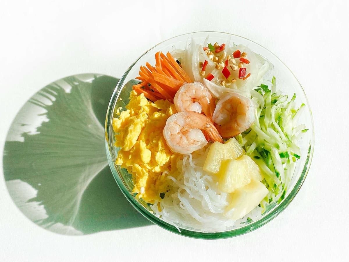 투명 볼에 담긴 샐러드. 새우, 곤약면, 스크램블 에그, 당근, 오이, 파인애플, 양파, 고추가 담겨 있다