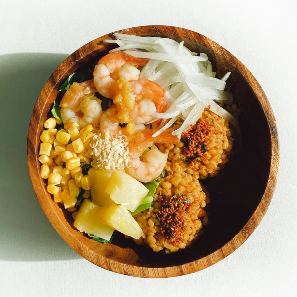 나무 볼에 담긴 포케를 위에서 내려다본 사진. 새우, 옥수수, 파인애플, 무순, 곡물이 담겨 있다